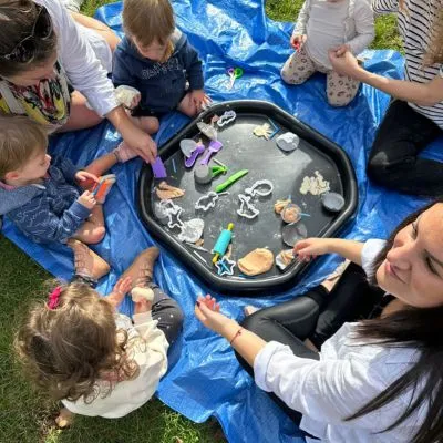 Children exploring a messy-play tray outdoors at a Shaping Little Minds session